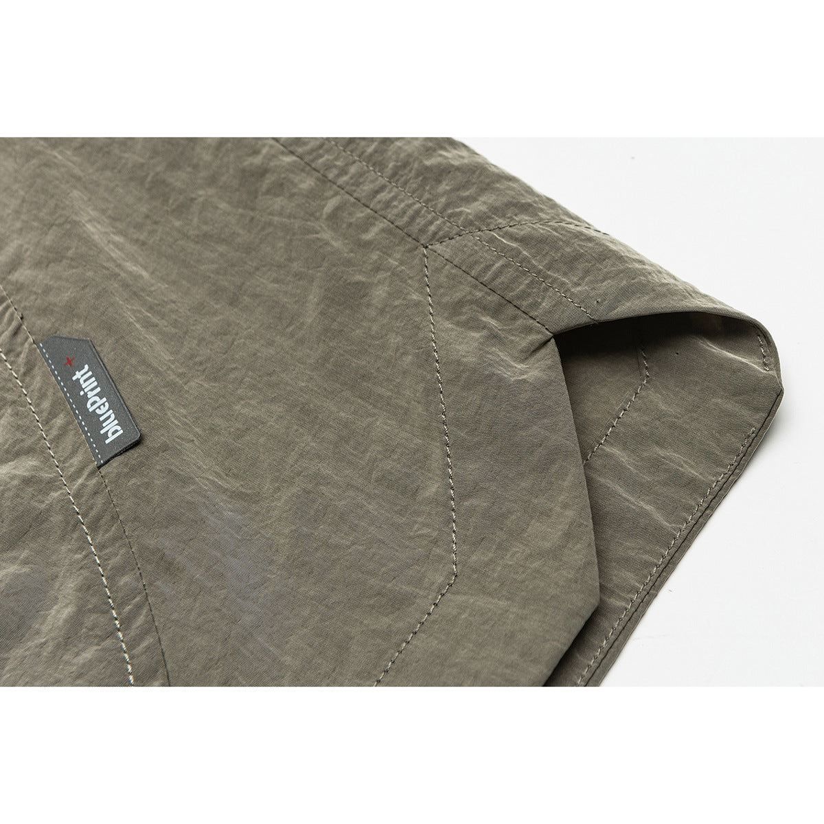 Close-up of olive-gray shorts showing stitched panels, a hem and a small Palladium label.