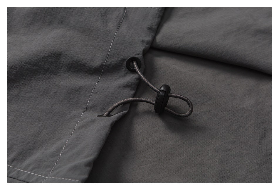 Close-up of a black elastic drawcord and toggle on charcoal gray fabric.