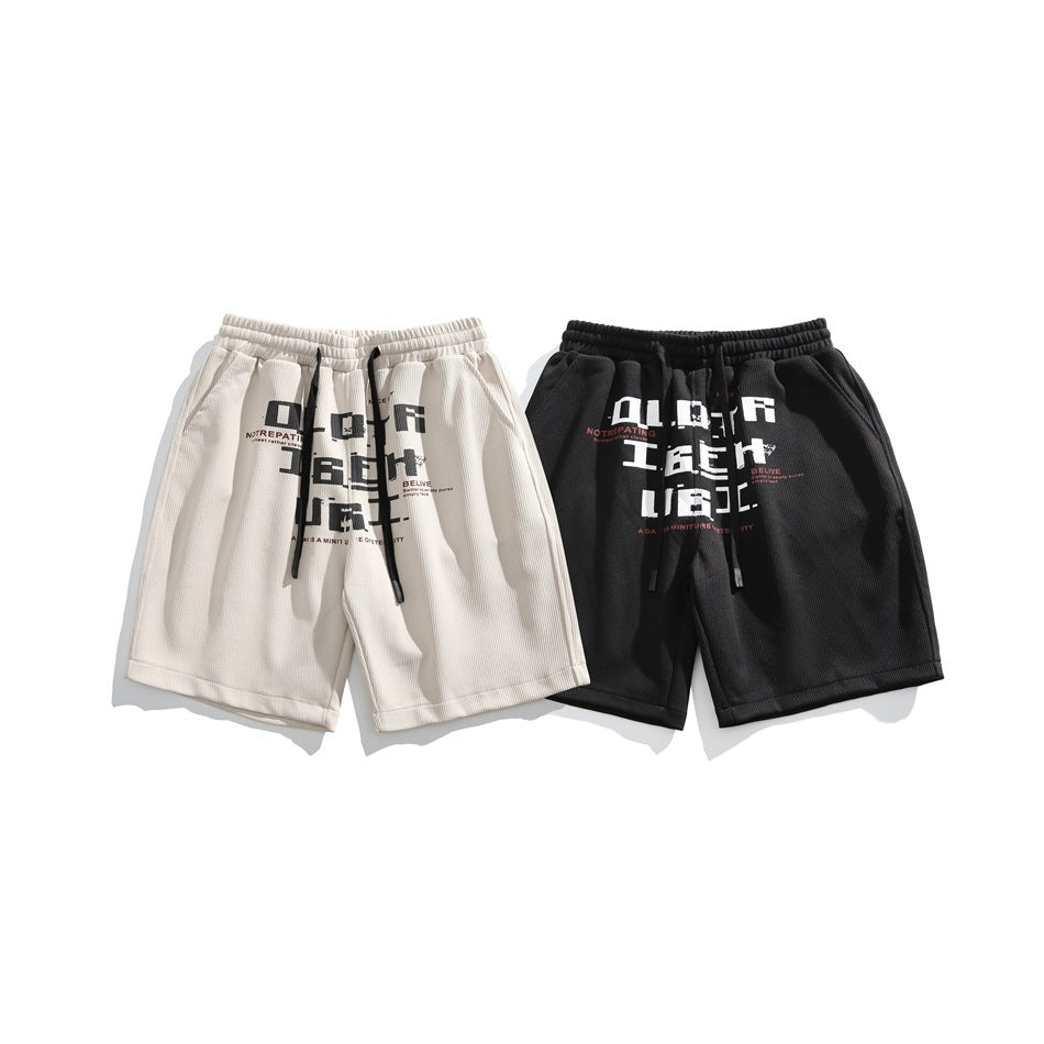 Light beige and black shorts shown together, each with a drawstring waist and contrasting text graphic.