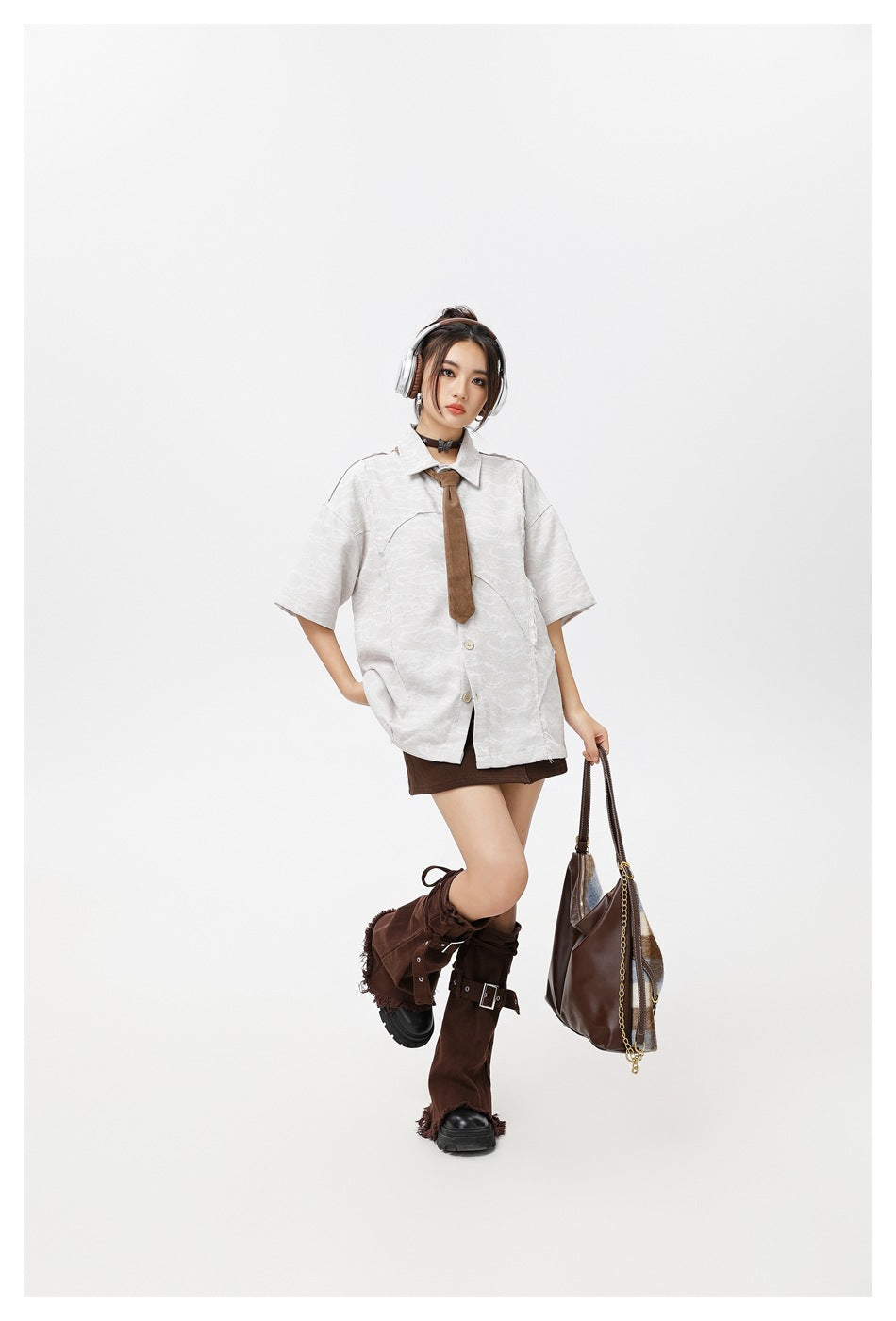 Full-length model wearing a pale gray patterned oversized shirt with a brown tie and dark brown skirt.