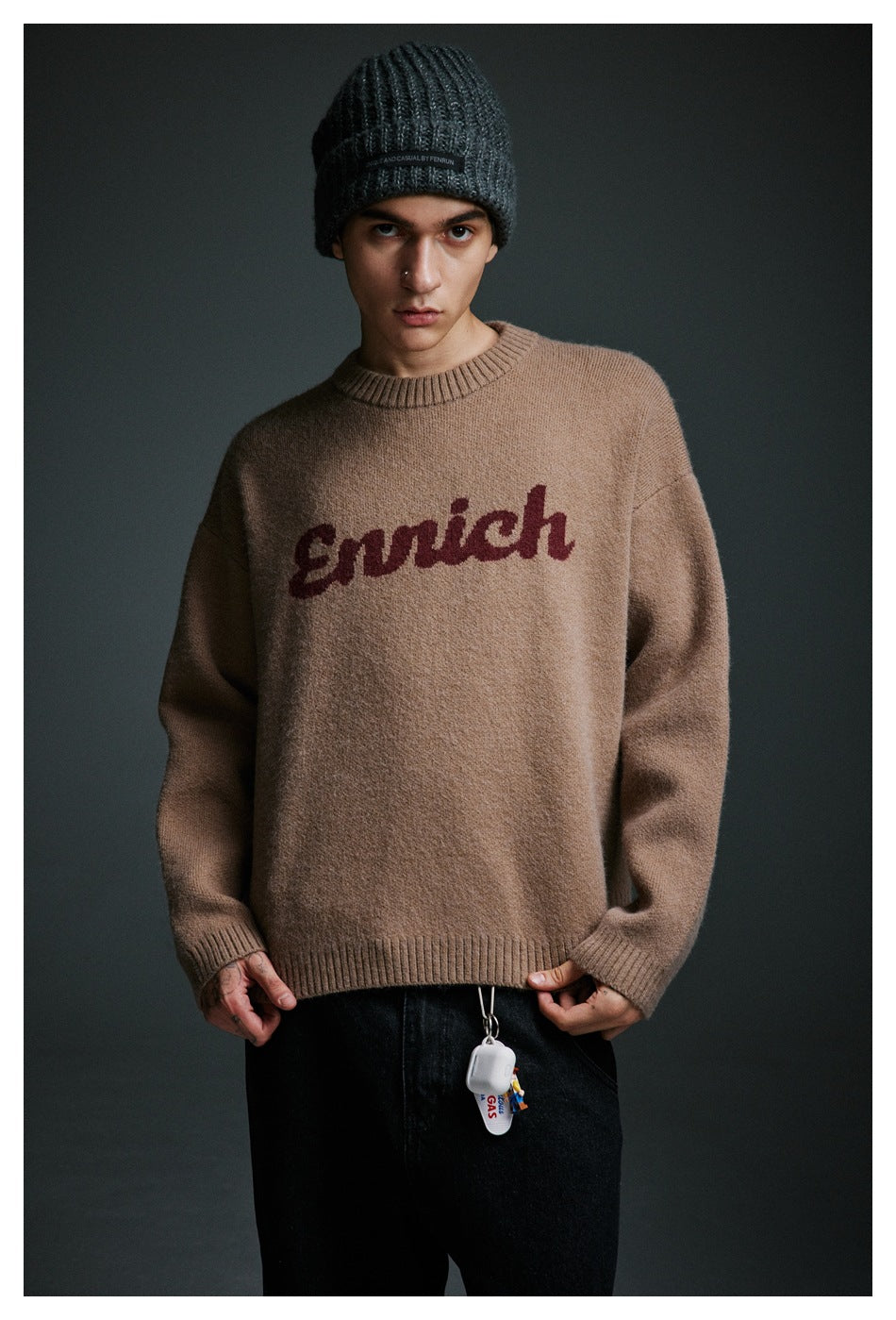 Front view of a model in a taupe crewneck sweater with burgundy script lettering, black jeans, and a charcoal beanie.