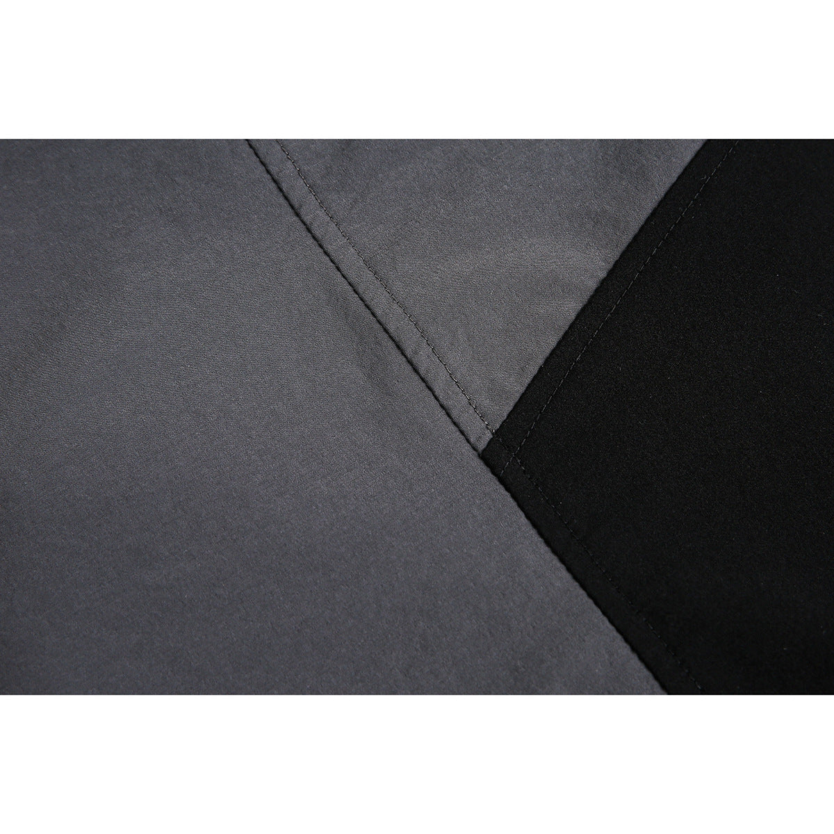 Close-up of a diagonal stitched seam joining charcoal-gray and black jacket panels.