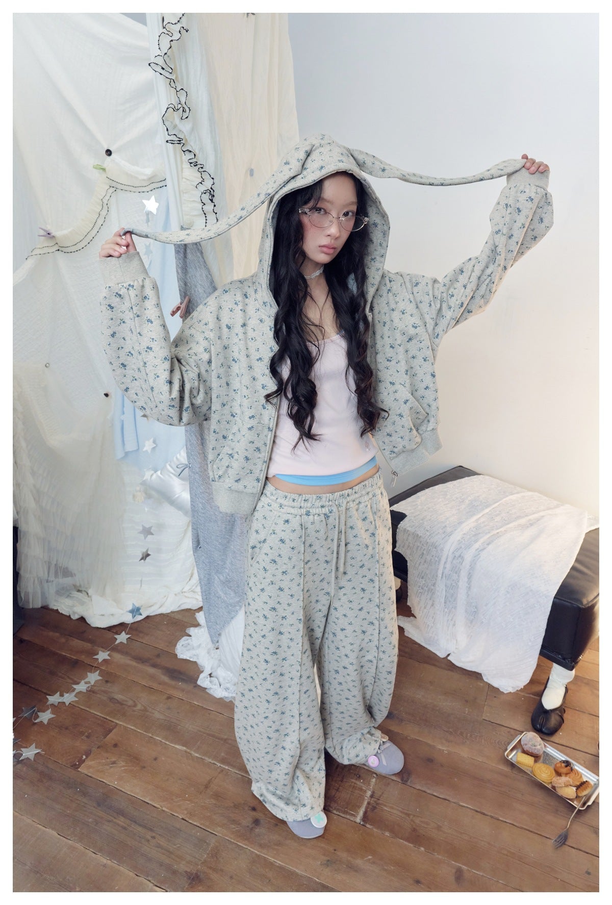 Model holding the long bunny-ear hood extensions of a gray blue-floral zip hoodie, worn with matching pants