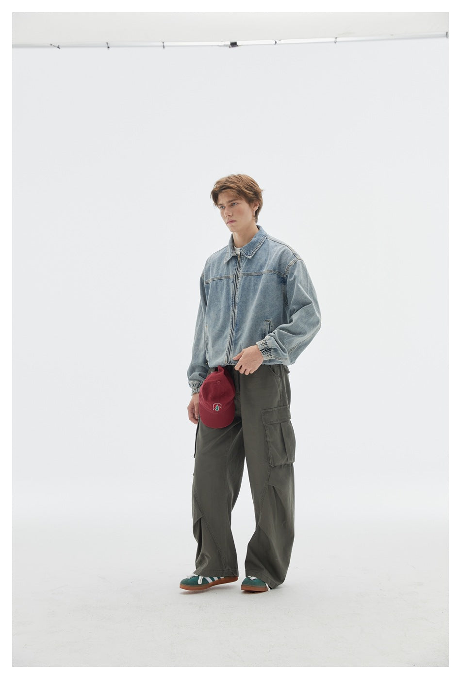 Model wearing gray-green wide-leg cargo pants with a light denim jacket and red cap, angled view
