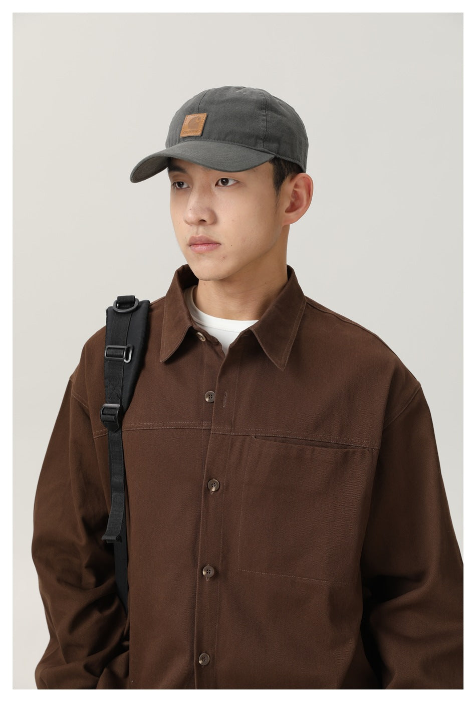 Close view of a model wearing a dark brown button-up shirt with a chest pocket and a gray cap.
