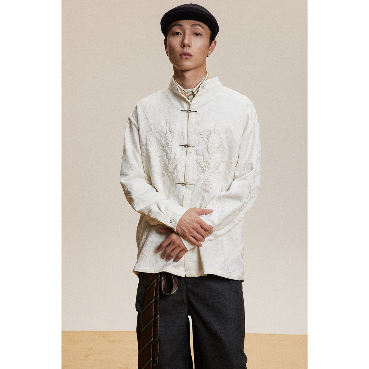Model wearing an ivory stand-collar jacket with bamboo embroidery and metal frog closures, shown from the front.