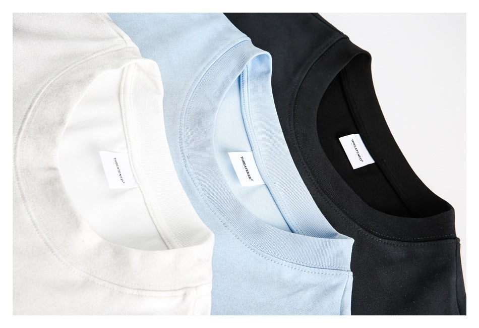Close-up of white, light blue, and black T-shirts arranged together, showing their crew necks and inner labels.