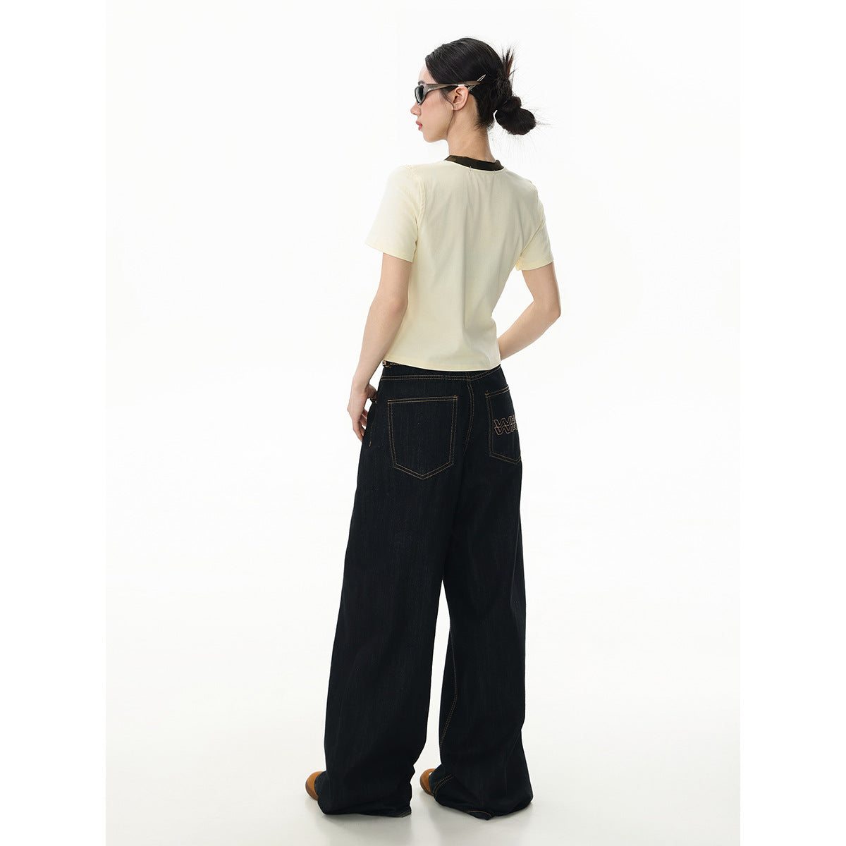 Model shown from behind in an ivory T-shirt and dark wide-leg jeans with prominent back pockets.