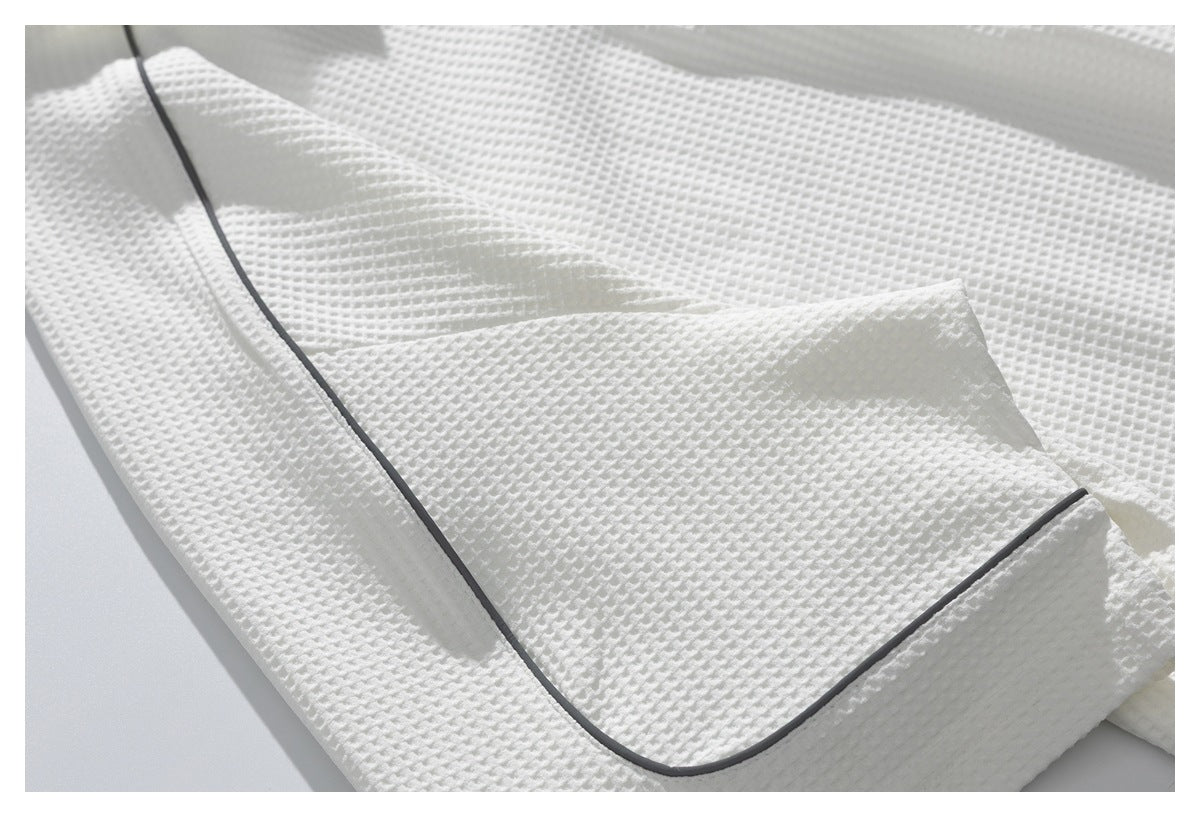 Close-up of white textured garment fabric with dark gray piping along an edge.