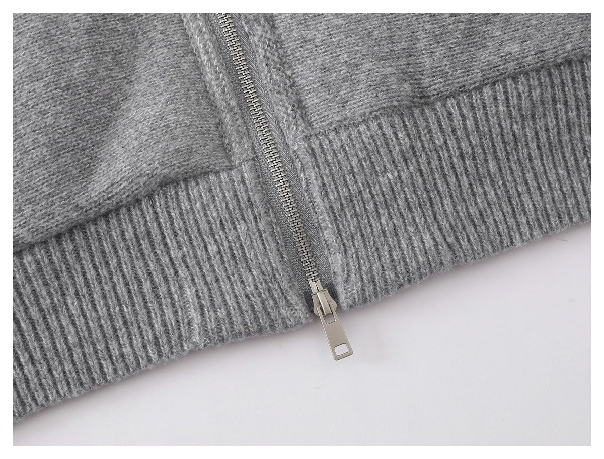Close-up of a metal zipper ending at the ribbed hem of a gray knit garment.