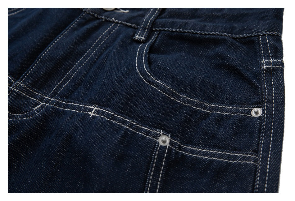 Close-up of dark indigo jeans showing the curved front pocket, coin pocket edge, and contrast stitching.