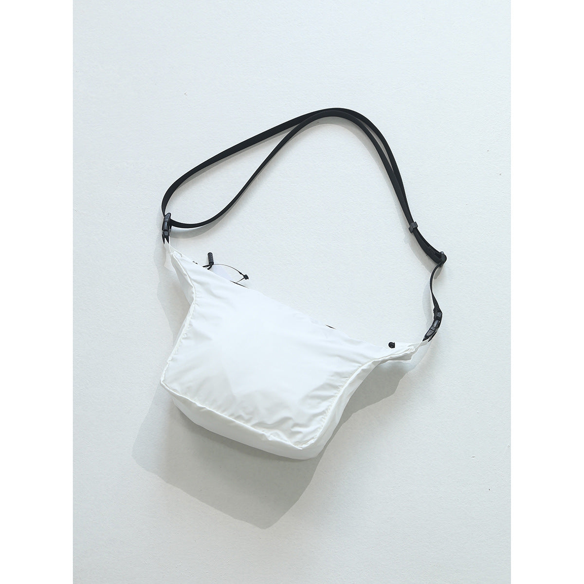 White crossbody bag with black adjustable strap and side-release buckles on a light background
