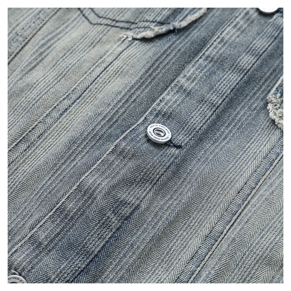 Close-up of a silver jacket button against textured blue-gray denim and visible stitching.
