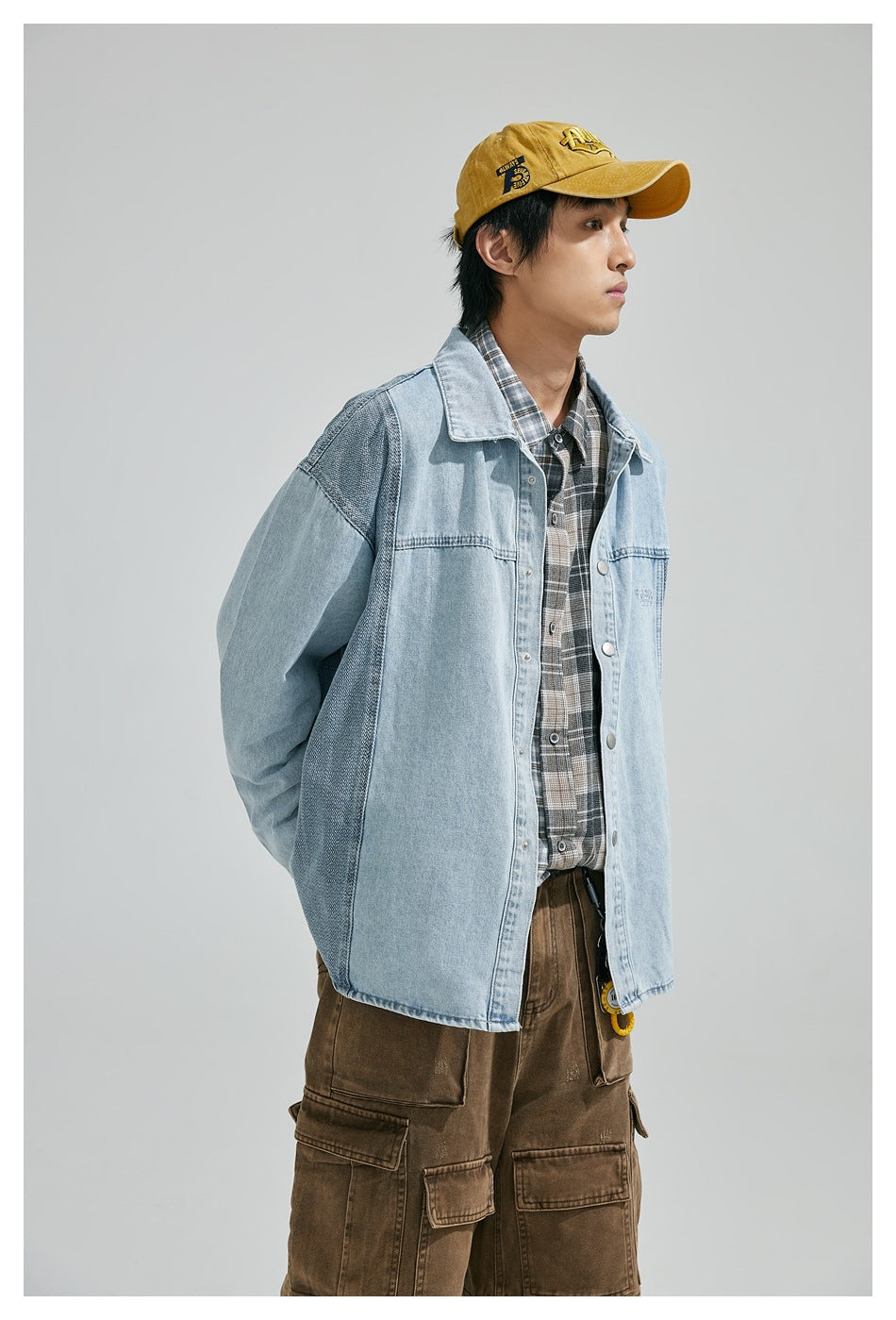 Model in a light-blue denim jacket with darker contrast panels, shown with a plaid shirt and brown cargo pants.