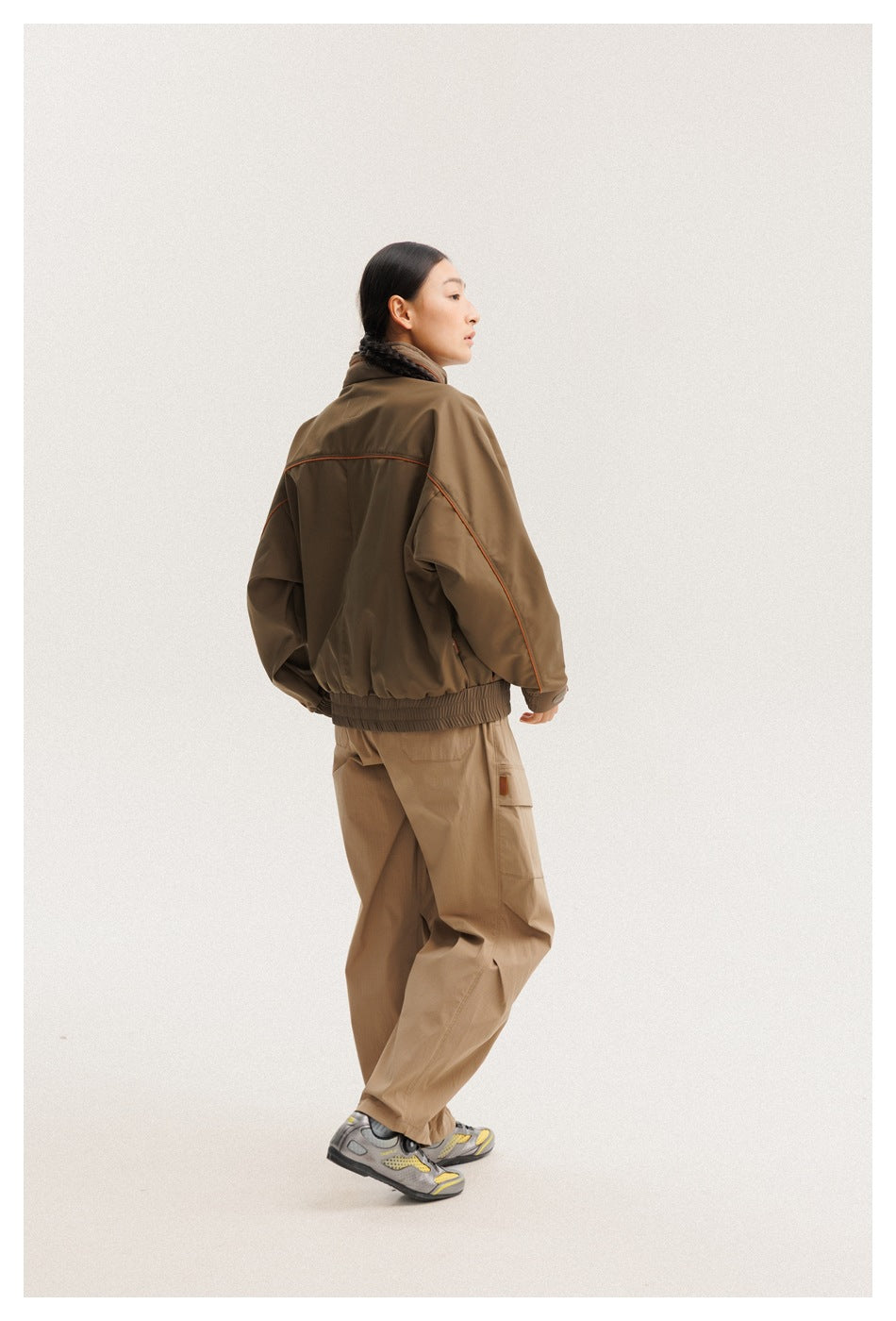 Model showing the back of a brown jacket with orange piping and an elastic hem.