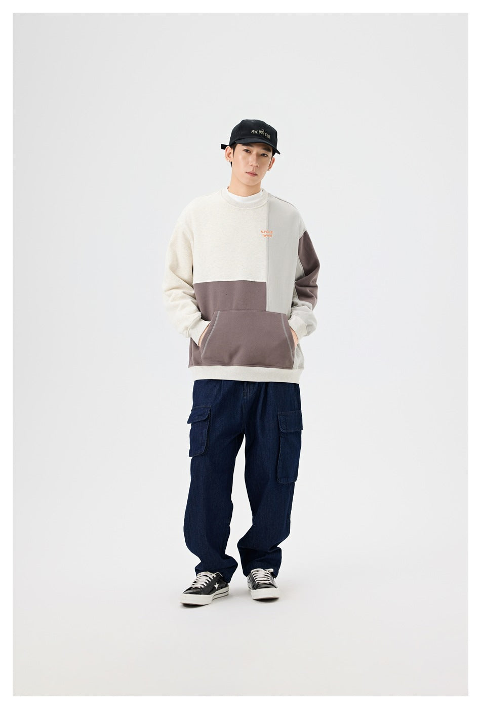 Full-length front view of a person wearing a cream, gray, and taupe color-block sweatshirt with navy cargo pants.