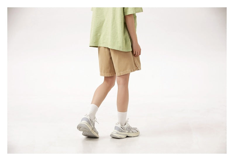 Cropped rear three-quarter view of a person wearing tan shorts and a pale green T-shirt.