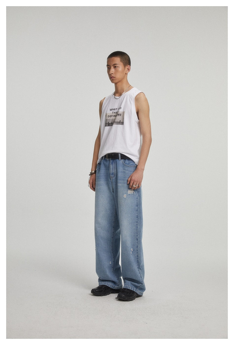 Three-quarter view of a model in a white graphic sleeveless shirt and loose distressed blue jeans.