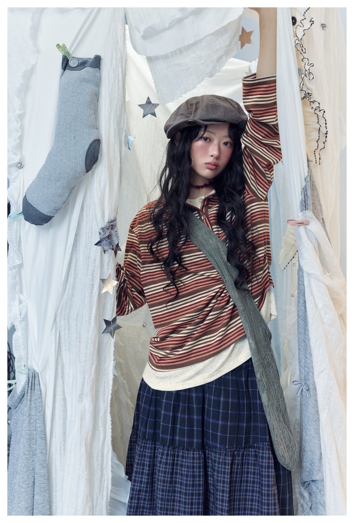 Model wearing a striped long-sleeve henley with a navy plaid tiered skirt and loose blue jeans.