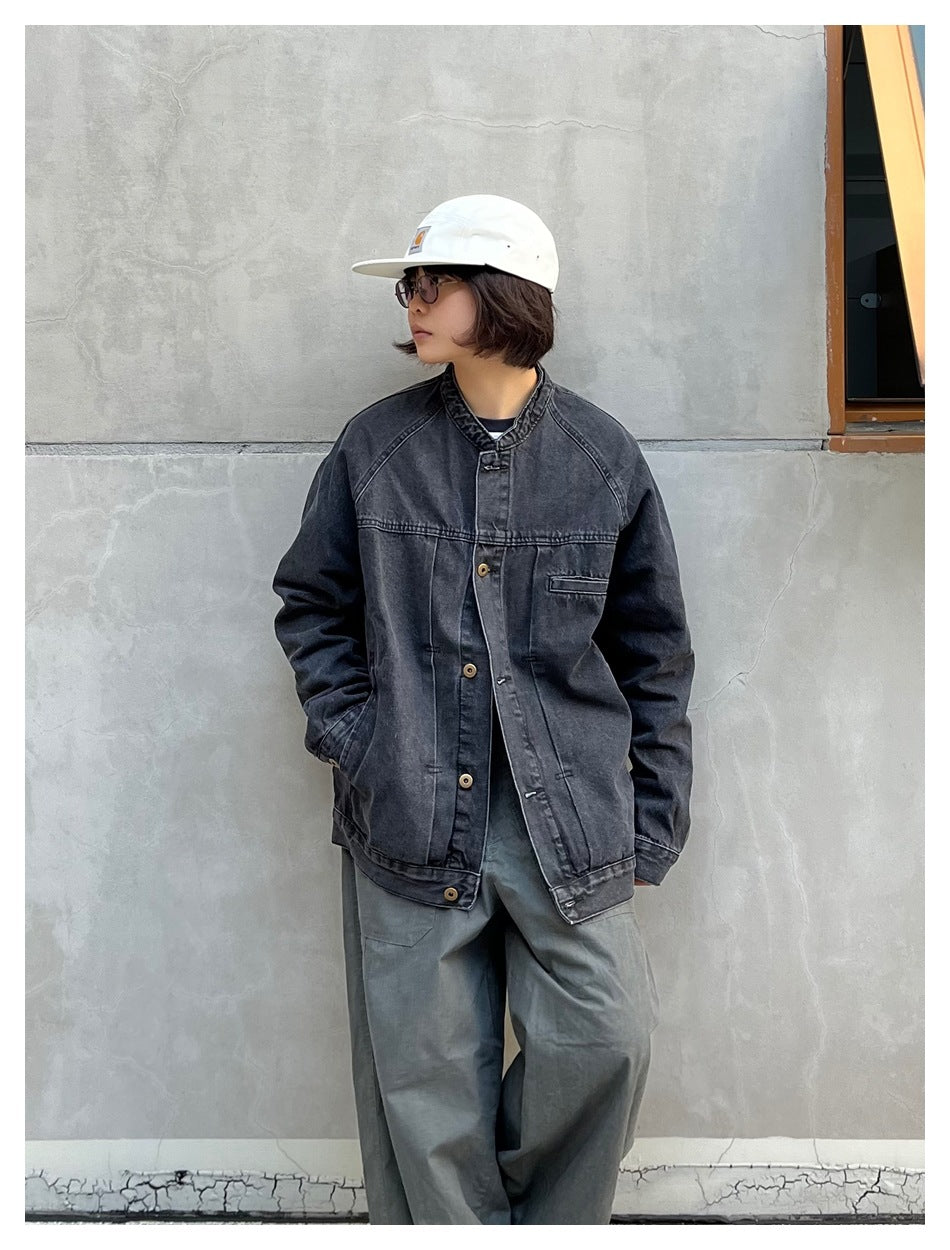 Person wearing a faded black denim stand-collar jacket with hands in pockets, gray wide pants and a white cap