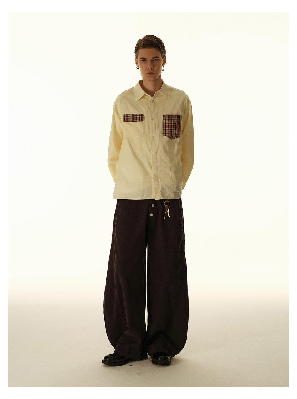 Full-length model wearing a pale cream button-up shirt with two plaid chest pockets and loose black trousers.