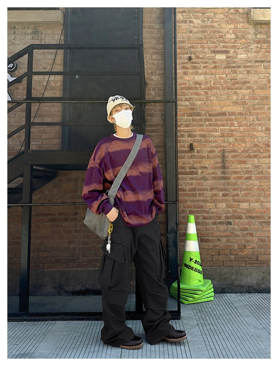 Model wearing loose black cargo pants with large side flap pockets and a purple patterned sweatshirt.