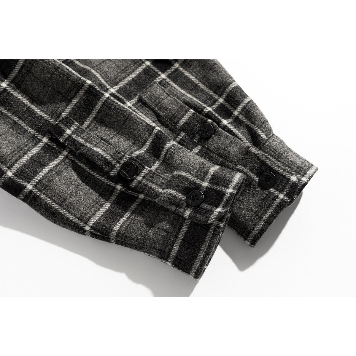 Close-up of a buttoned cuff on a charcoal gray shirt with a white plaid pattern.