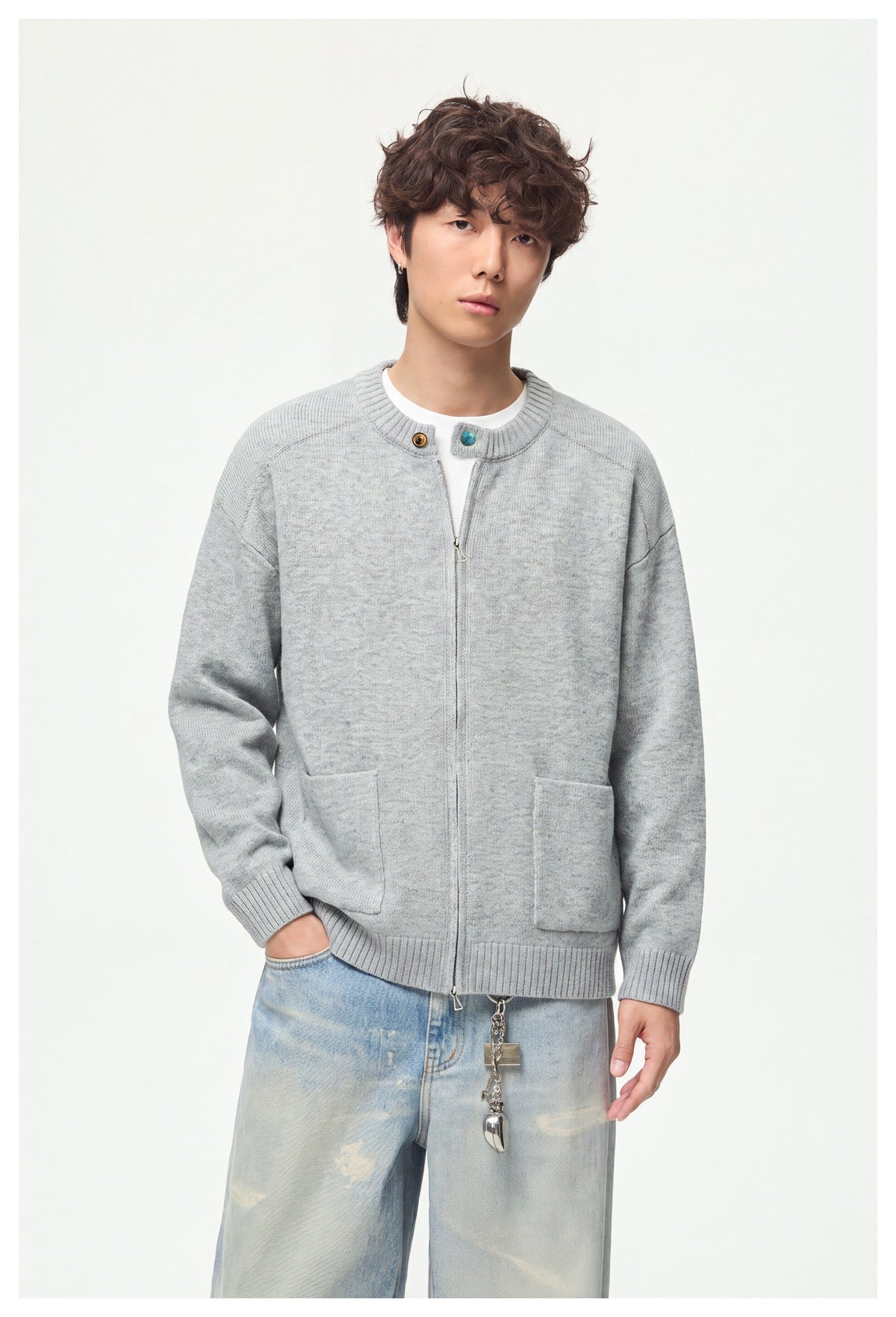 Model wearing a light gray zip-front knit cardigan with ribbed trim, patch pockets, and contrasting buttons.