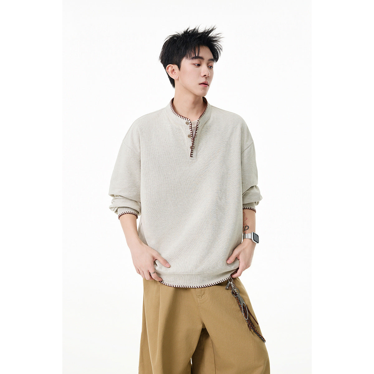 Man wearing a cream pullover with a short button placket and dark contrast stitching, sleeves pushed up.