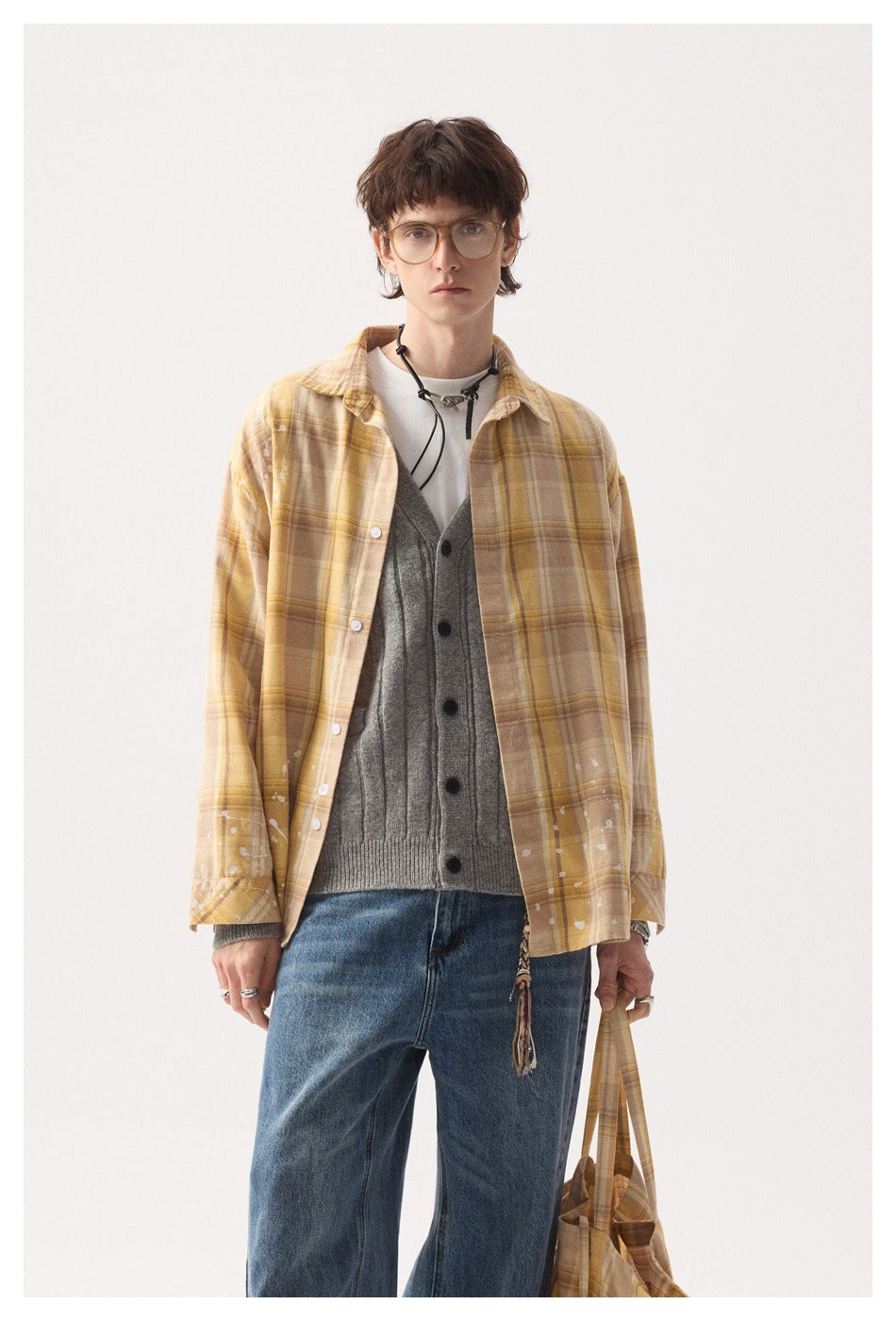 Close-up of a model in the yellow plaid paint-splatter shirt worn open over a gray knit cardigan