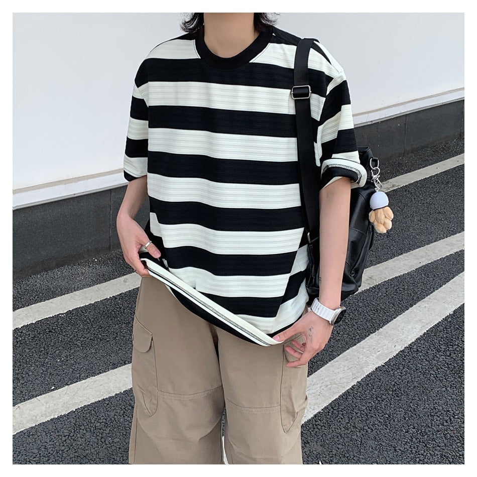 Person wearing a black and cream striped T-shirt, lifting the hem to show the inner edge, with khaki cargo pants