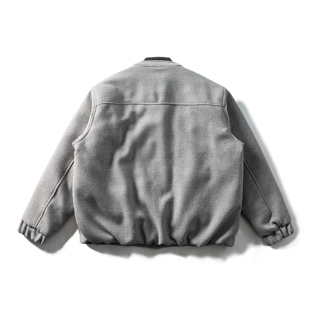 Back view of a gray jacket laid flat, with long sleeves, a horizontal shoulder seam and gathered cuffs.