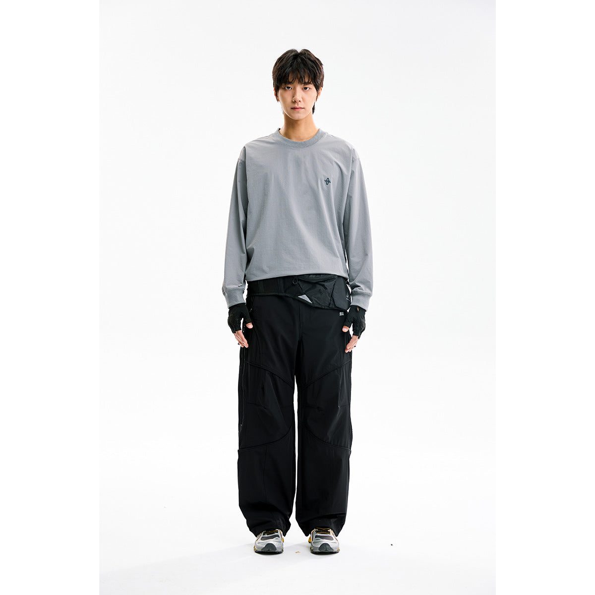 Front view of a model wearing a gray long-sleeve crewneck with a small chest emblem and loose black pants.