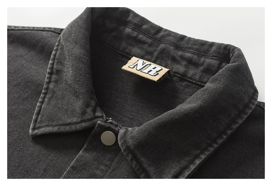 Close-up of a black denim jacket collar, silver snap, and NB neck label.
