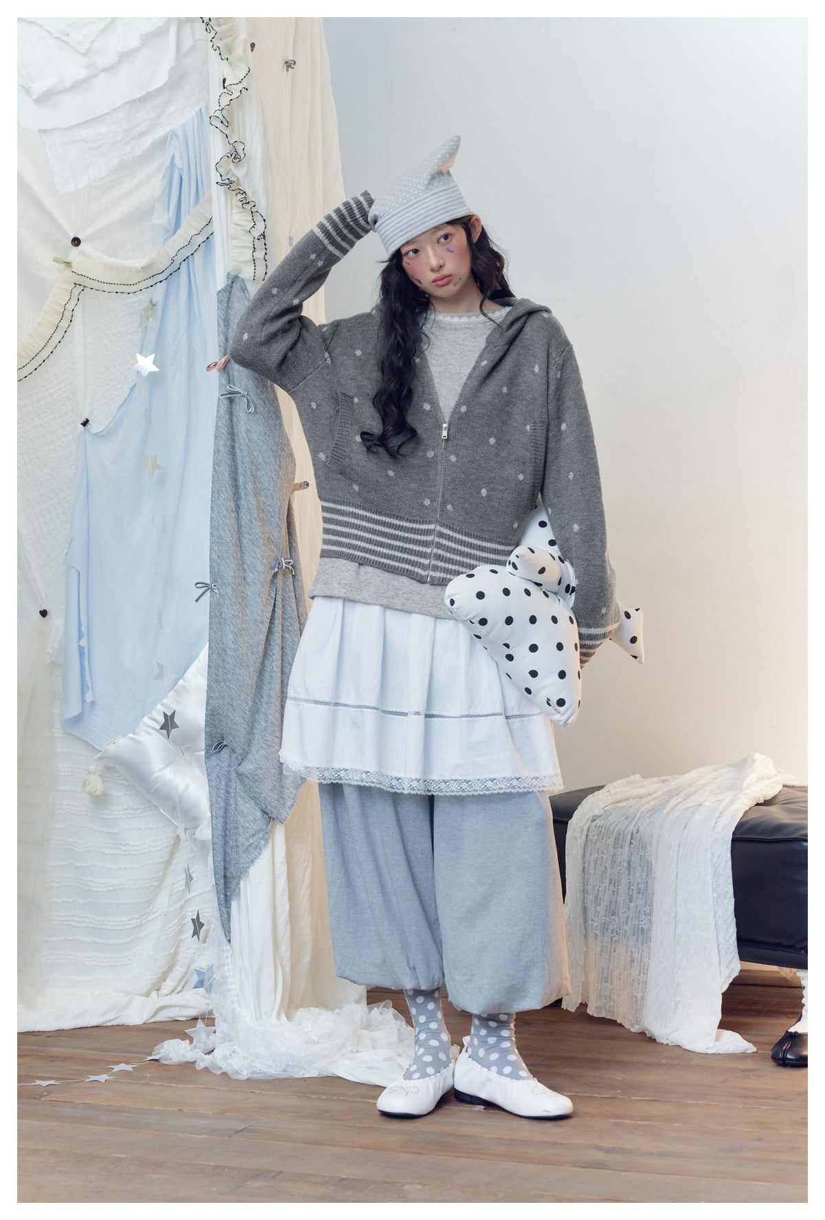 Model posing in a gray spotted zip hoodie, white layered skirt and loose gray pants.