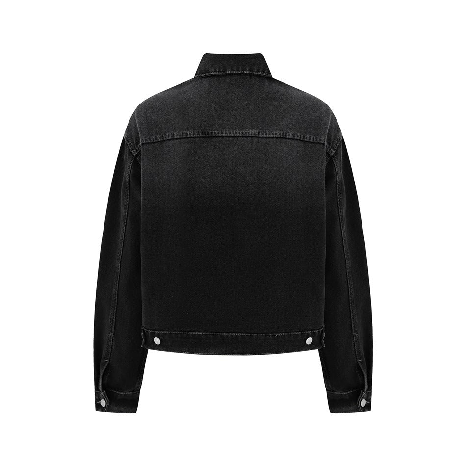 Back view of a black denim jacket with a plain panel, yoke seam, buttoned cuffs, and hem tabs.