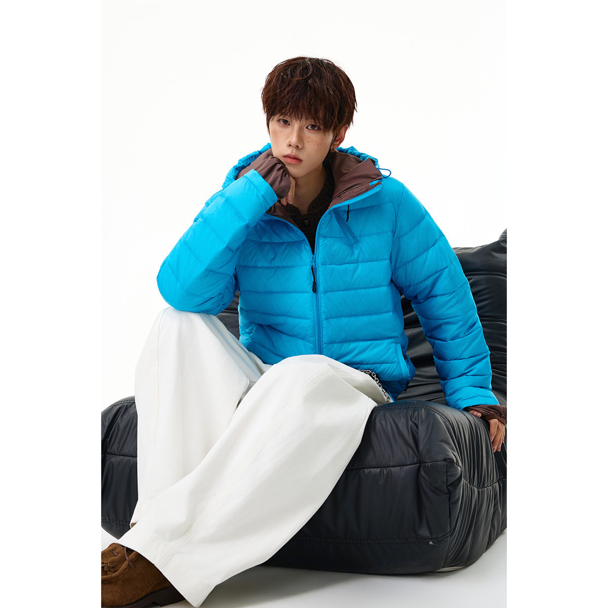 Seated model wearing a bright blue hooded puffer jacket and white wide-leg trousers.