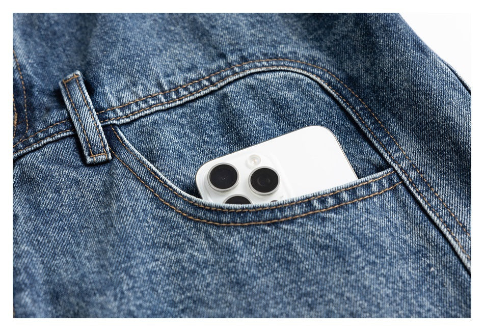 Close-up of a white smartphone tucked into the curved pocket of blue denim jeans.