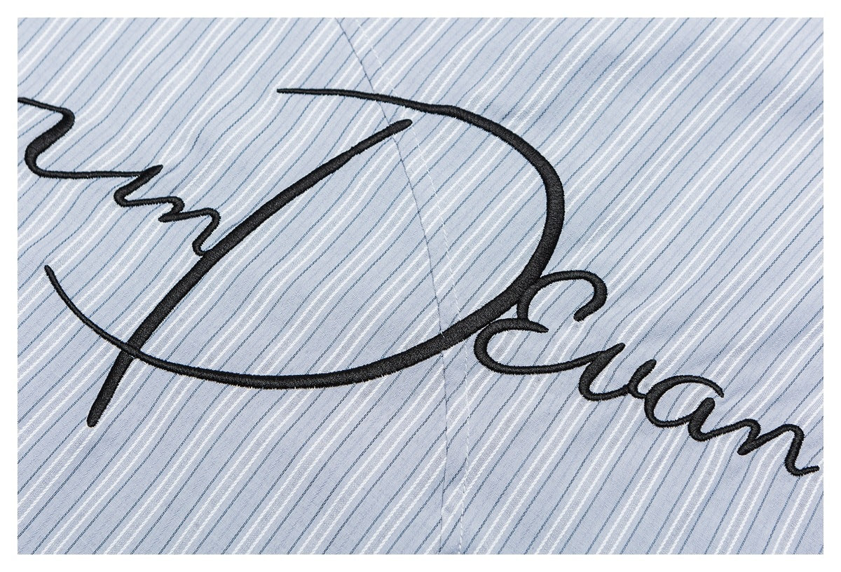 Close-up of black cursive embroidery on pale blue fabric with fine white and dark blue stripes.