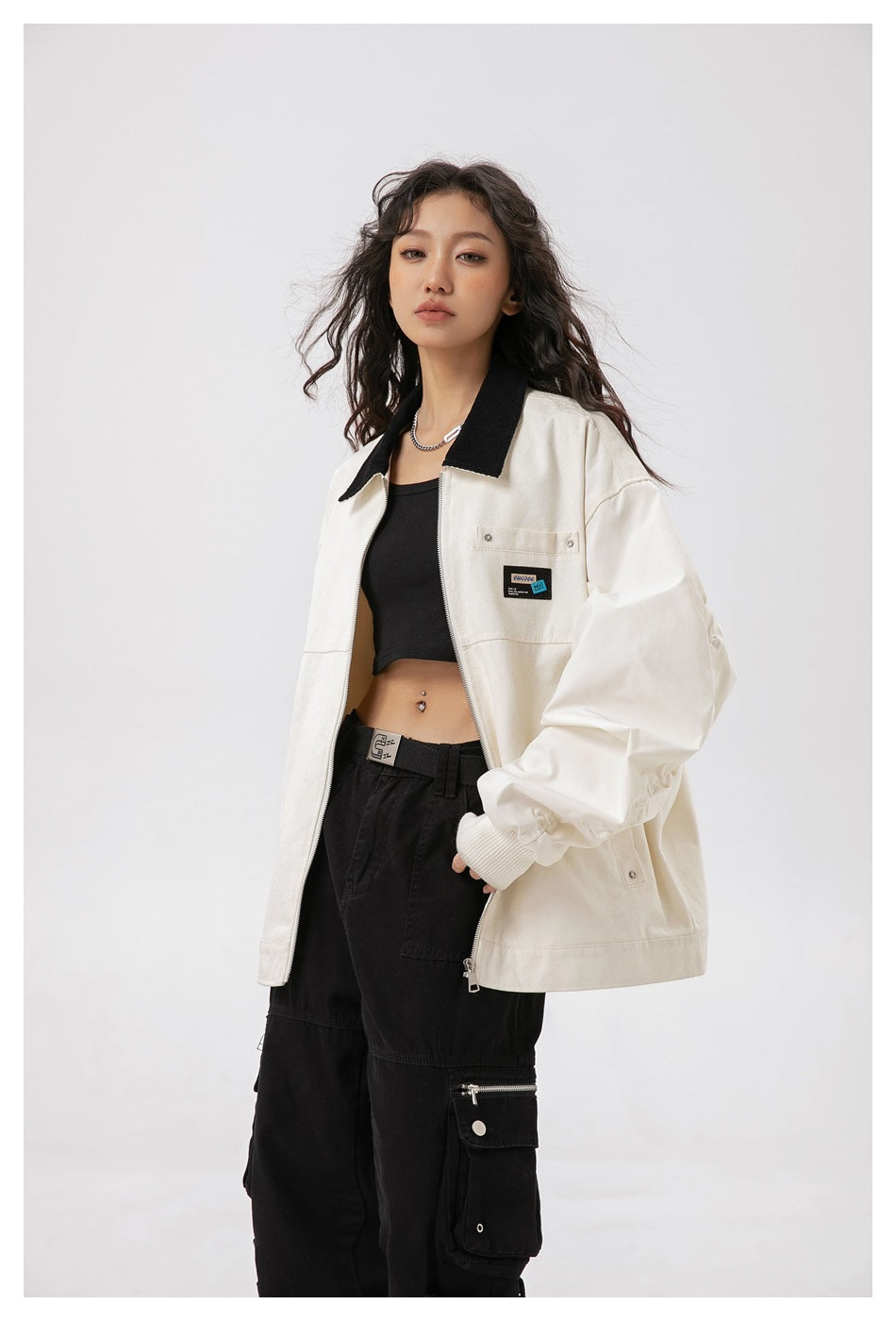 Model wearing an open ivory jacket with a black collar, showing its zip front and chest patch.
