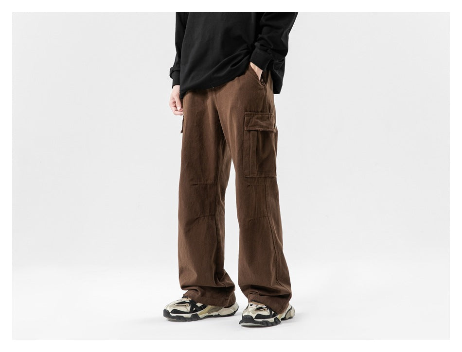 Cropped model wearing loose brown cargo pants with a flap thigh pocket and wide legs, shown from the front.