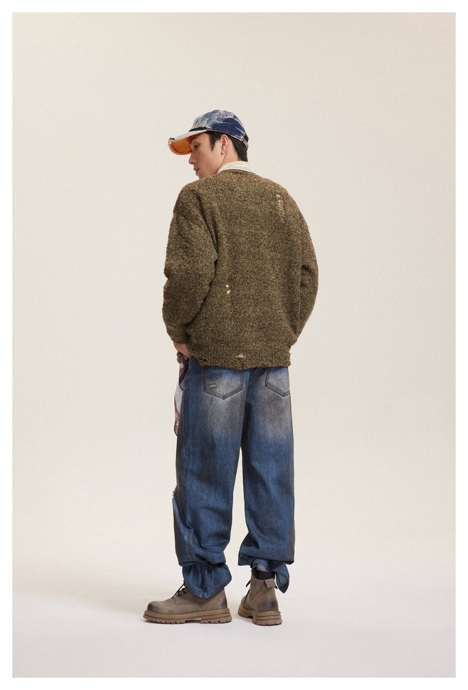 Rear view of a model wearing an olive-brown textured sweater with distressed details and loose blue jeans.