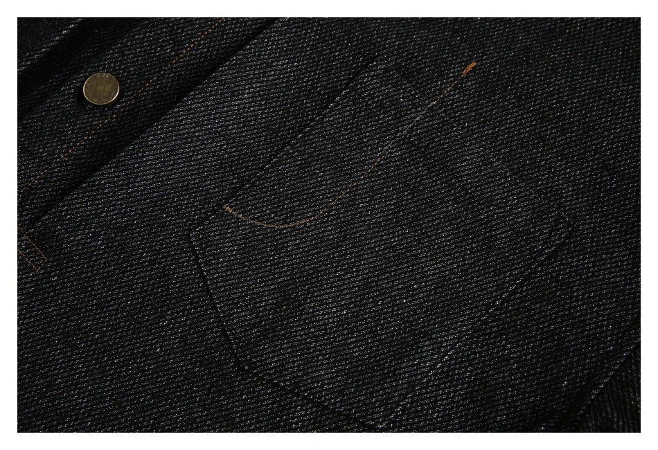 Close-up of black denim with orange stitching, a metal button, and a curved pocket seam.