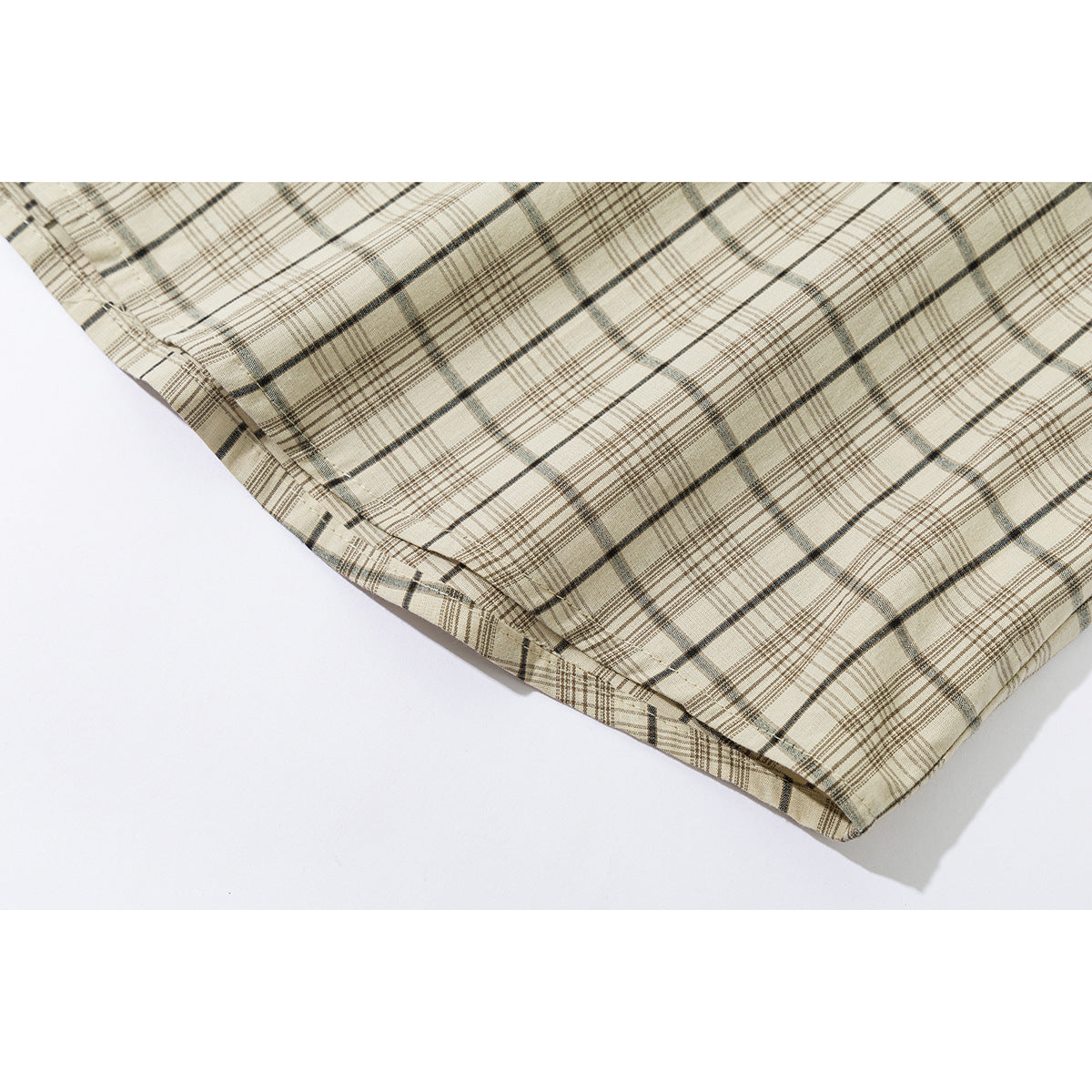 Close-up of the beige plaid shirt's curved hem and stitching.