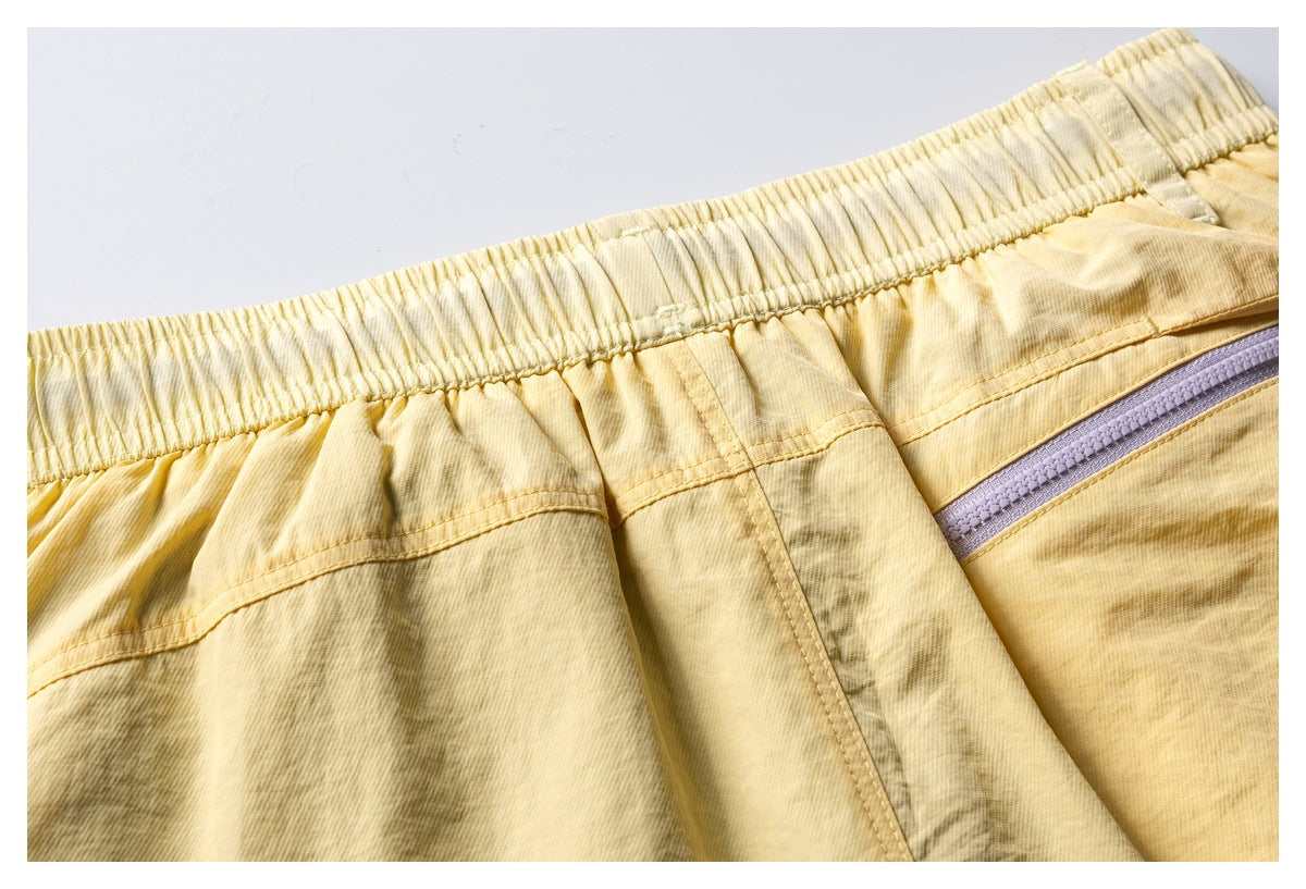 Close-up of the elastic waistband and seams on pale yellow patterned shorts, with a lavender zipper at the side.
