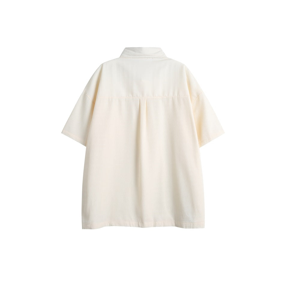 Back view of an off-white short-sleeve collared shirt with a yoke seam and center pleat.