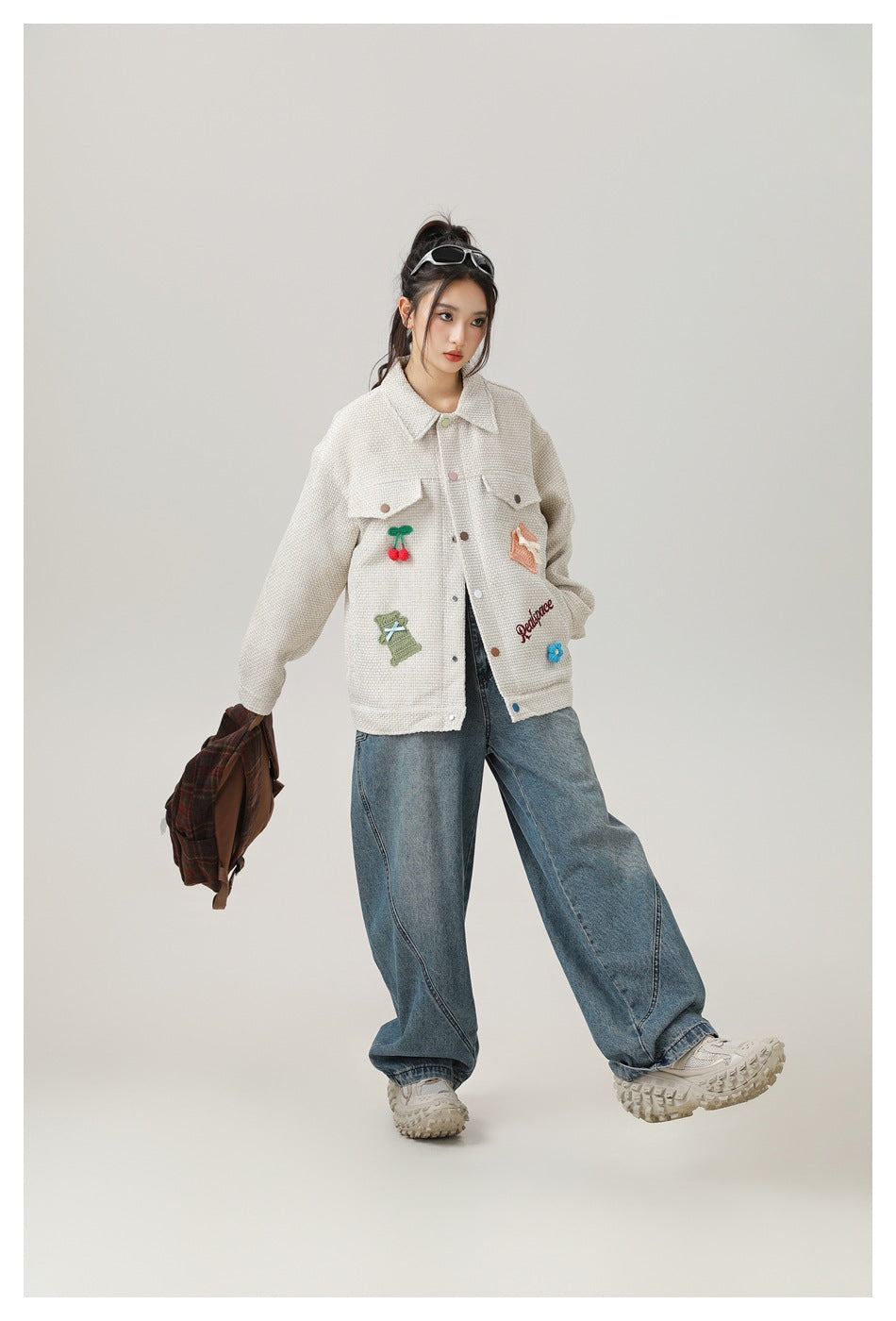 Model in a cream embroidered jacket and wide-leg blue jeans, posing with one leg extended.