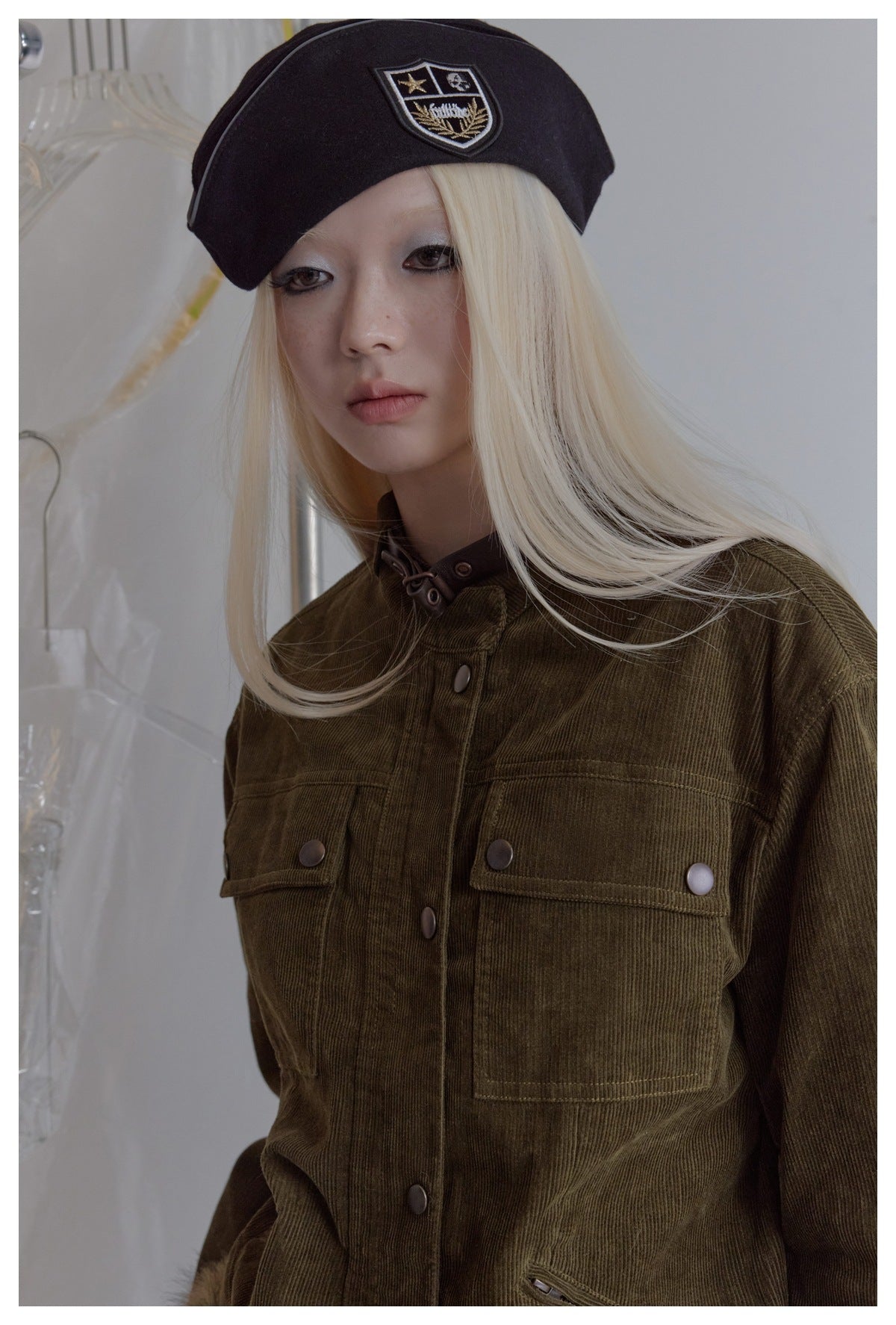 Close-up of a model wearing an olive jacket with snap-button chest pockets and a black beret.