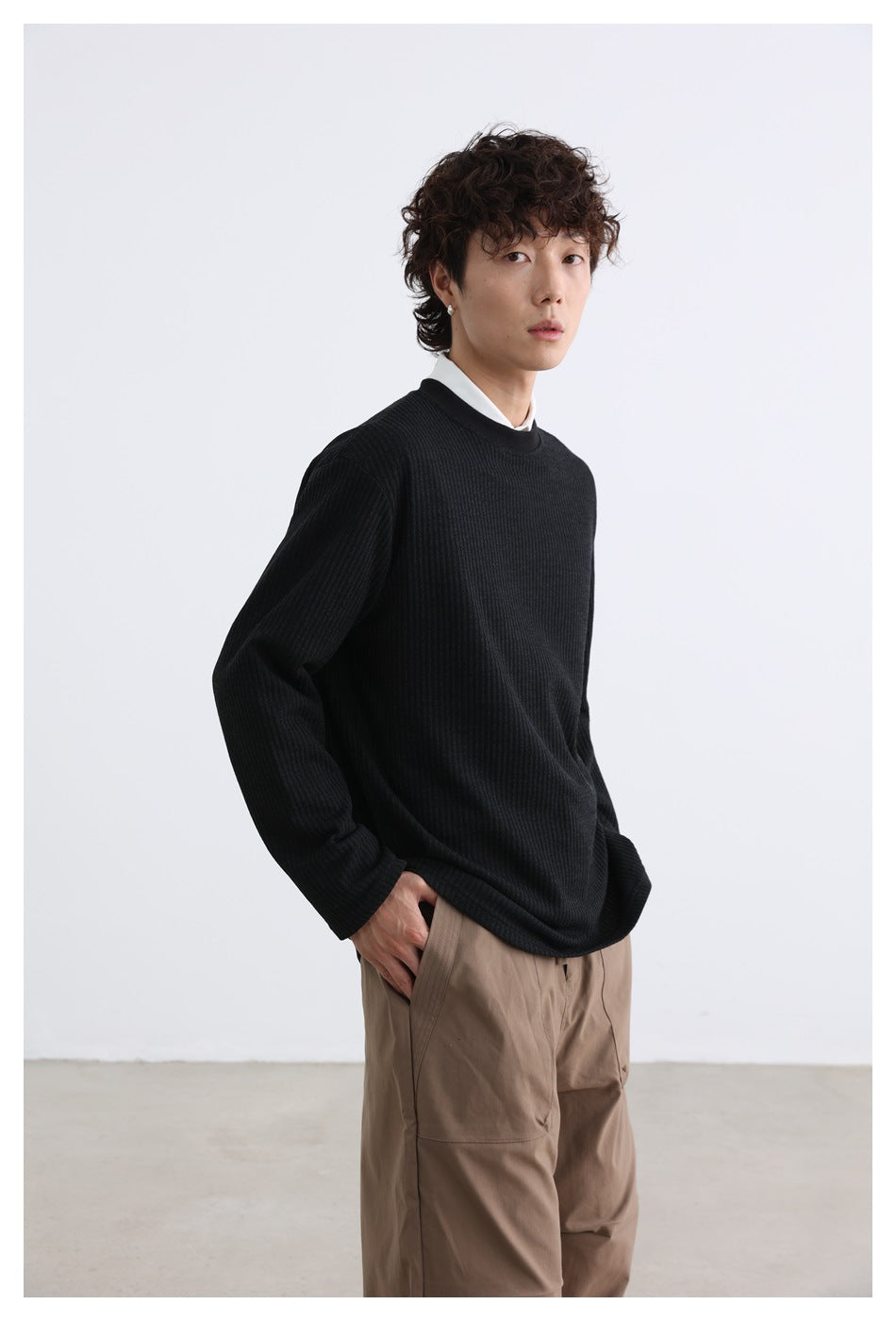 Three-quarter view of a model wearing a black ribbed crewneck over a white shirt.