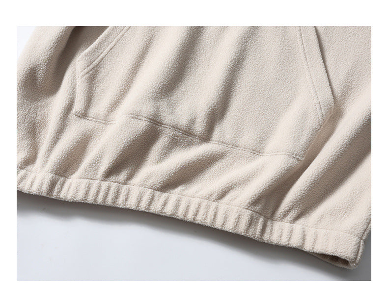 Close-up of a cream hoodie’s kangaroo pocket and gathered elastic hem.